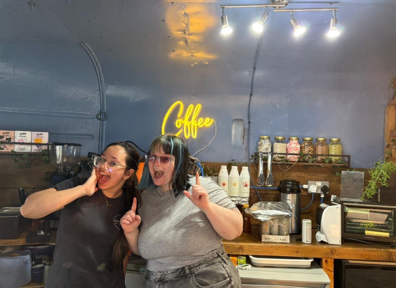 The two founders of Sea’s and Sky’s inside their finished coffee trailer, under a neon Coffee sign
