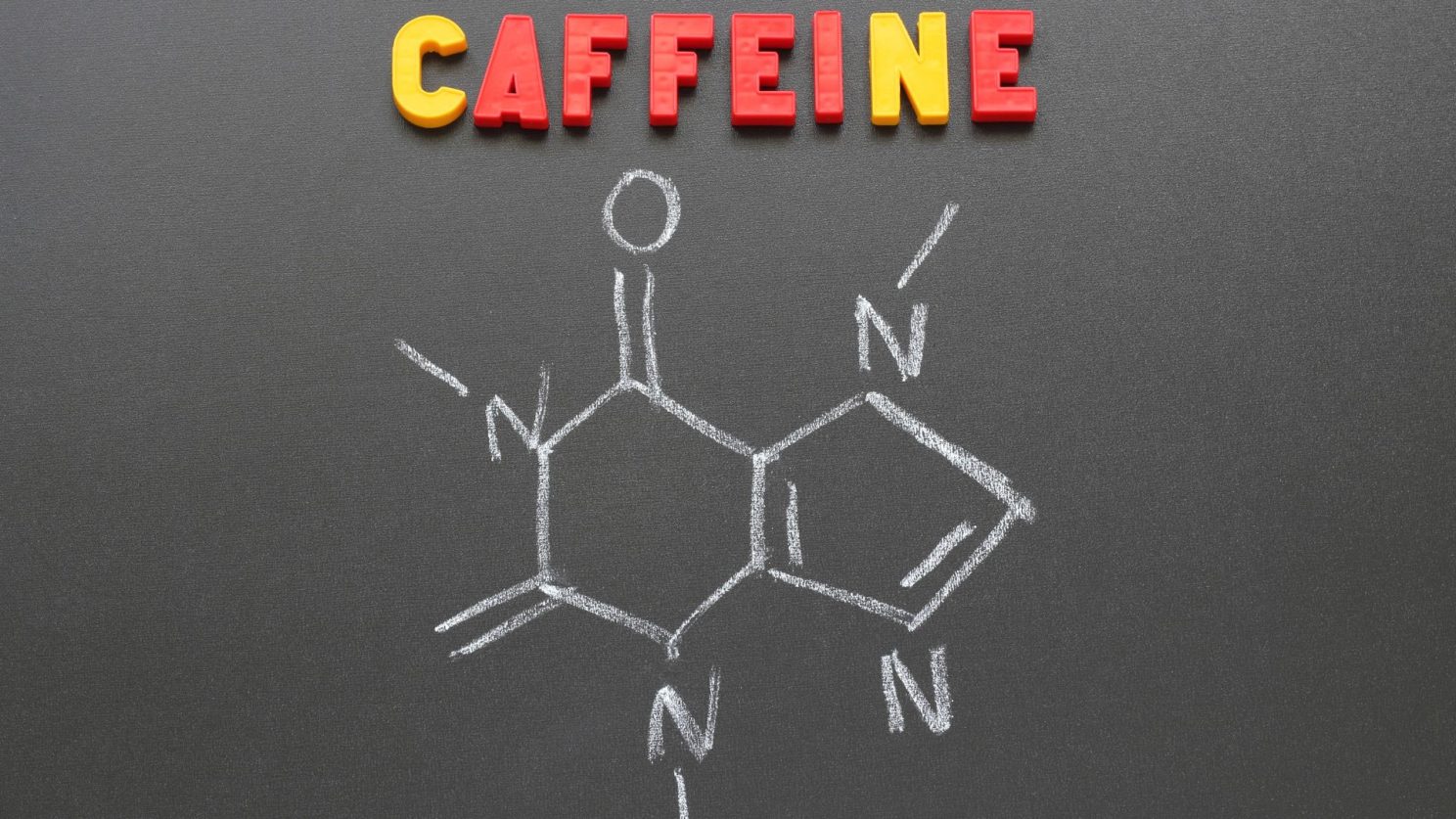 The word CAFFEINE in coloured letters above the caffeine molecule drawn in chalk on a blackboard