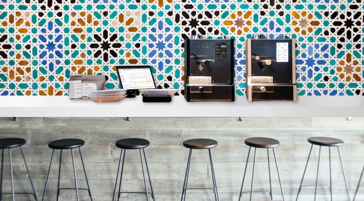 A café counter with two automated espresso machines and a tablet-based ordering system