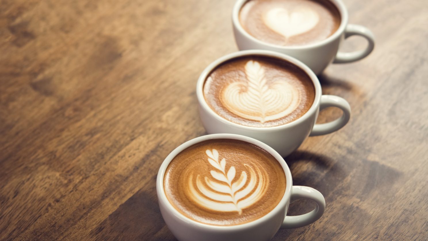 Three cups of coffee with latte art on a wooden table